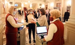 Staff in red and white uniforms and masks check tickets in the foyer