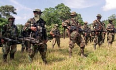 men in gear with guns, ammo and their faces obscured stand in a grassy field