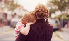 Young boy resting on mother’s shoulderA young boy being held by his mother with his head resting on her shoulder, looking down a suburban street.