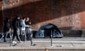 People walking past a tent pitched next to a brick wall