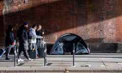 People walking past a tent pitched next to a brick wall