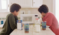Two children wait with anticipation by a microwave
