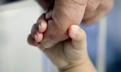 A close-up of a baby's hand clasping an adult finger
