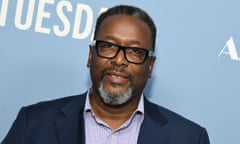 Middle-aged Black man wearing black-framed glasses and open necked shirt, smiling at press event