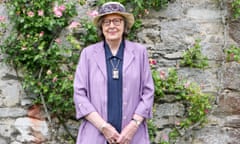 penelope lively standing by a garden well with climbing roses