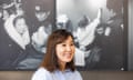 A young Mongolian woman sitting on a leather sofa wearing a blue shirt in front of a series of large black and white news photos hung on the wall