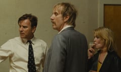 In a movie still, the actors stand in a hallway beside a grungy white wall, all looking to their left. McGregor looks concerned, Ifans looks curious, and Boyle is puffing on a cigarette.