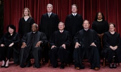 Nine people in black robes, five sitting, four standing behind them, smiling in front of a red curtain. One Black woman, two Latino women, one white woman, one Black man, four white men.