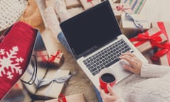 Aerial view of woman's hands doing Christmas shopping on a laptop, surrounded by gifts.