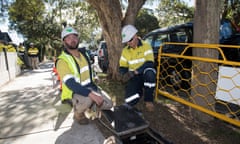 Two tradespeople wearing protective equipment install NBN in a suburban street