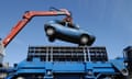 An old car being lowered into a car crusher by a crane, seen from below