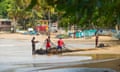 Three fishermen working on nets on a beautiful sandy beach fringed with palm trees, with small boats pulled on to shore behind them