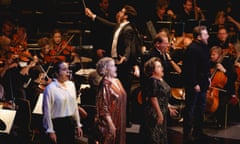 a line of singers at the front of a stage at the royal albert hall, behind them an orchestra and a conductor