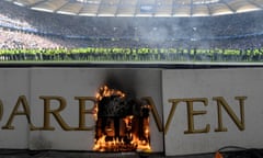 An advertising hoarding on fire as stewards are lined up across the pitch after trouble marred Hamburg’s relegation.