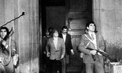 Men in civilian clothing carrying automatic weapons as they exit a building