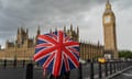 Pedestrians shelter underneath a union jack umbrella on a wet Westminster Bridge in London