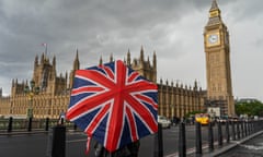 Pedestrians shelter underneath a union jack umbrella on a wet Westminster Bridge in London