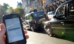 A man holds a smartphone displaying the Uber app in front of London black taxis