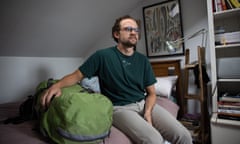 Man sits with a green bag wearing a green t=shirt inside a bedroom