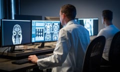 Male radiologist analysing the MRI image of the headRear view of male radiologist looking at the MRI image of the head on his monitor and analysing it.