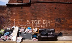 Ashton-under-Lyne in Greater Manchester: view of a brick wall with fly-tipped rubbish in front of it, including broken furniture and a leather sofa. Graffiti on the wall reads Stop Dumping Here, Grass, and Rat.