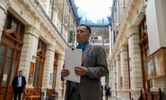 man wearing tweed suit and blue shirt holds papers