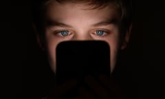 A teenage male looks at the screen of a mobile phone in the dark
