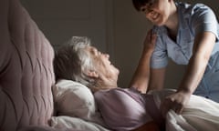 Care worker chatting to senior woman in bed. Model and property released
