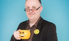 dean burnett smiling wearing a smiley badge and holding a smiley cup