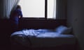 A young man by a blue-lit bed looking out the window