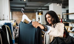 A woman shopper holding up a navy blouse on a clothes hanger.