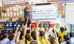 Sam Wollaston standing by an interactive whiteboards in a classroom with young children sitting on the floor in front of him with their hands up