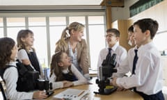 Happy students and teacher using microscopes in classroom