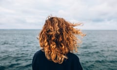 View from the back a woman with curly hair looks at the sea