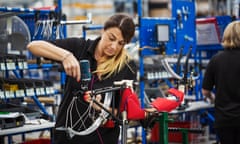 Female factory worker assembling a bicycle in a factory, working on the frame and wheels.