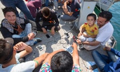 Refugees sitting by the shore charging their mobile phones.