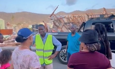 Man in hi-vis jacket with hands on hips talking to two others with back to camera with vehicle and mountains in background