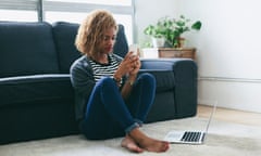 Young woman sitting on the carpet of living room looking at her smartphone