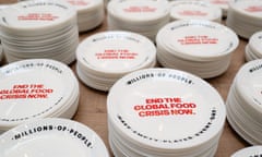 Empty plates laid out to symbolise the 733.4 million people living with hunger worldwide. The central message in red reads: End the global food crisis now. Round the edge is written: Millions of people have empty plates every day