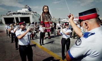 Piraeus municipal band accompany Little Amal, a giant puppet of a young Syrian refugee, as it leaves the Greek port for Italy. The 3.5m figure is on a 8,000km journey across Europe to highlight the plight of child refugees.