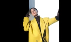 St Vincent in a white-lit stage set doorway in a yellow coat