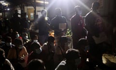 Lines of south Asian men under lights clutching papers