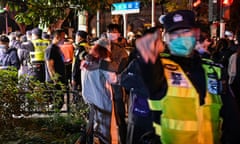 A police officer points a finger at the photographer as a man and woman hug in a large crowd of protesters and police