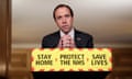 Matt Hancock at a podium reading 'stay home, protect the NHS, save lives' at a Downing Street briefing