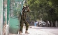 A man in combat fatigues stands by a mental door aiming a rifle at an unseen target