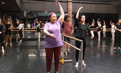 A woman in a purple T-shirt and maroon tights attends a ballet class.