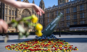 Hand holding flowers pointing to mock missile pointing at parliament and containing words ‘stop arming Israel’
