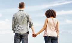 Young couple looking out to sea, holding hands.<br>GettyImages-136863942