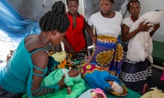 Four African women with small babies wait in a tent