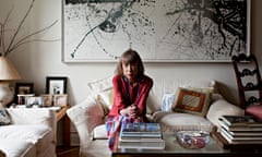 Joan Didion sitting on a sofa with a painting in the background a coffee table with books on in front of her.